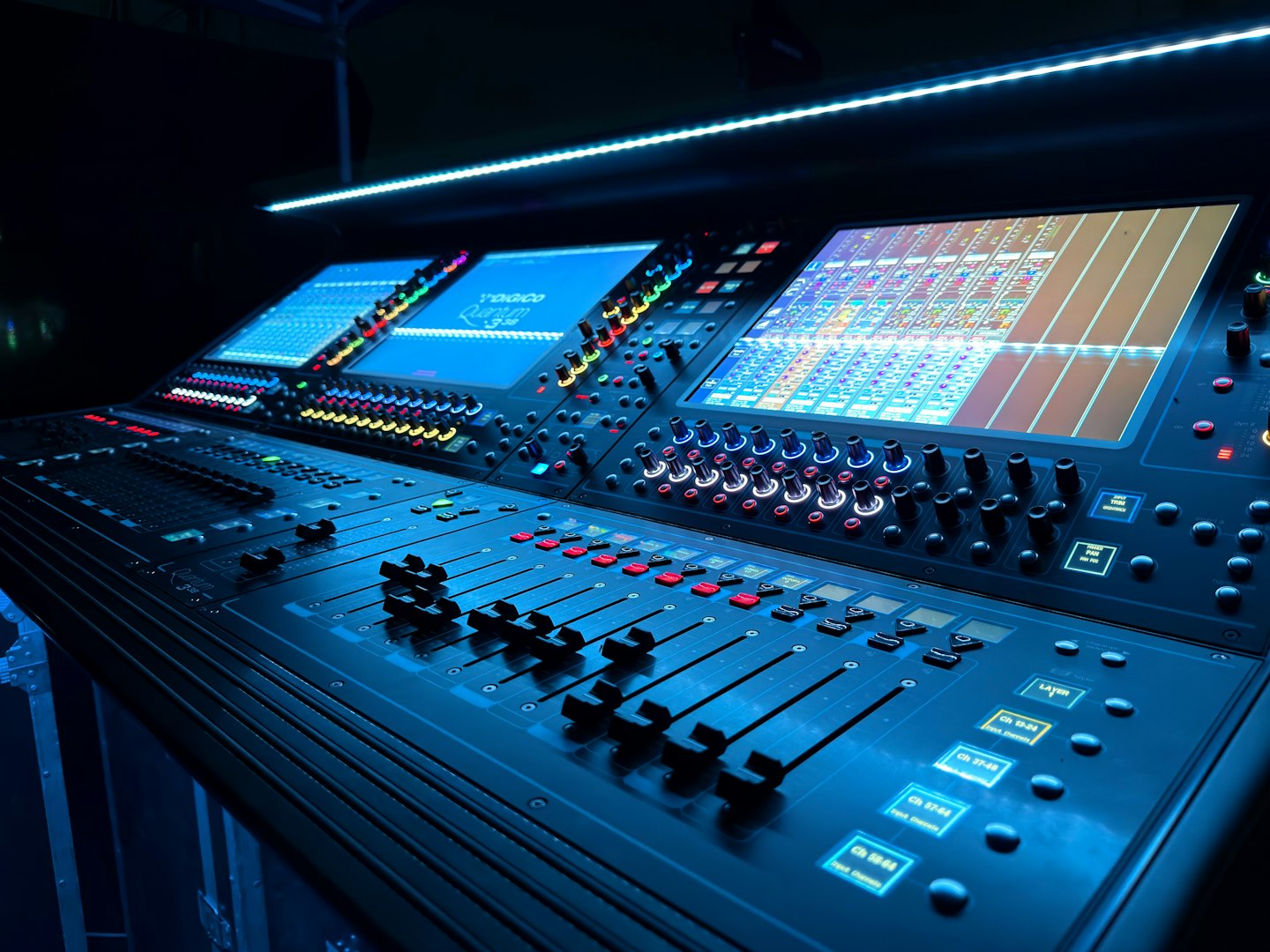 Digital audio mixing console with illuminated screens and faders.