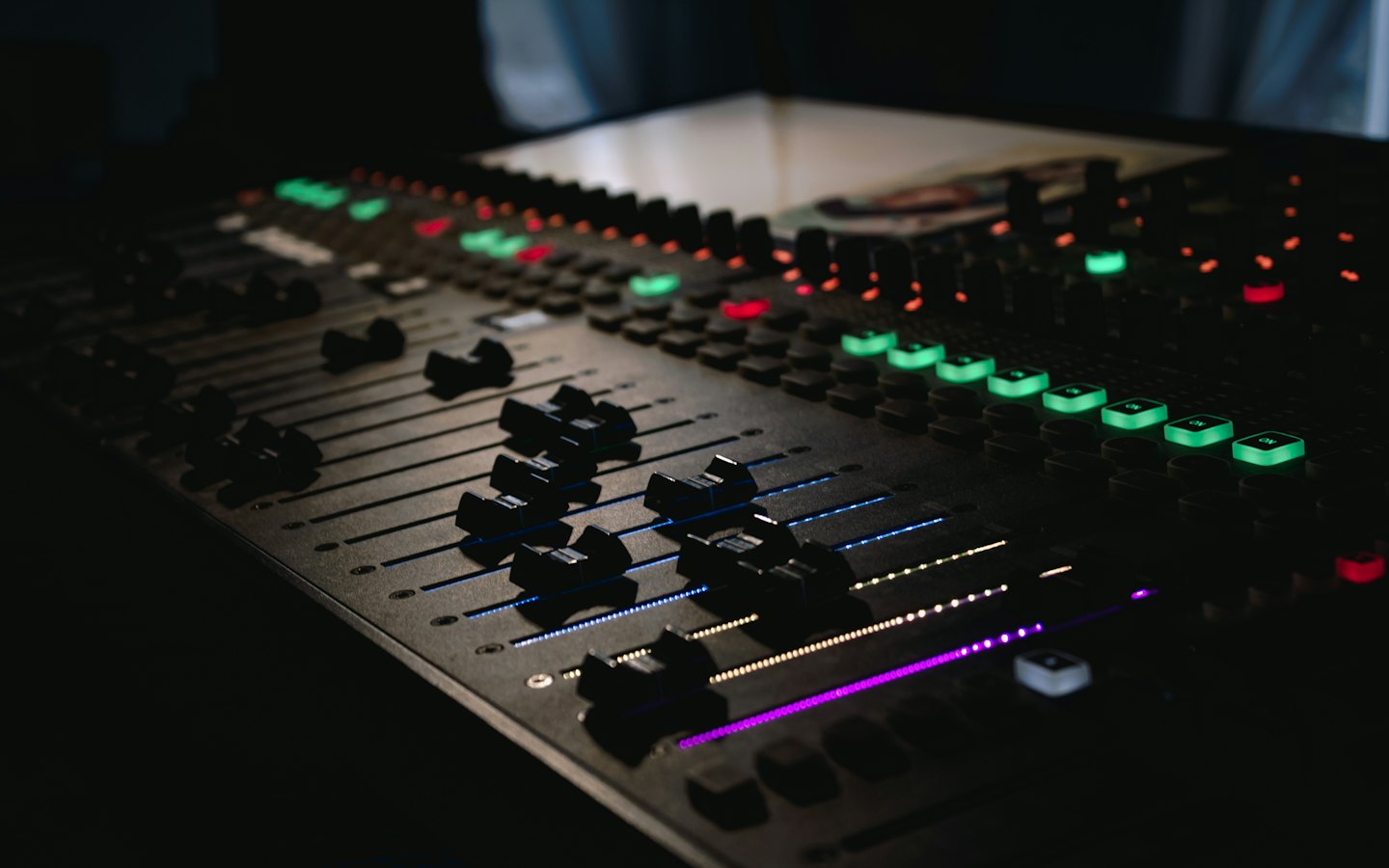 Audio mixing console with illuminated faders and buttons.